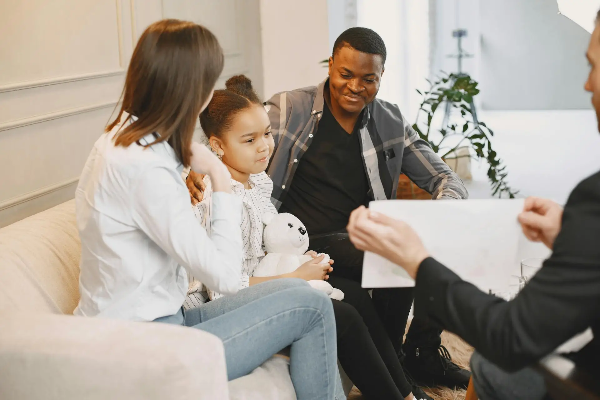 A child and her parents are sitting in a sofa in front of a physiatrist